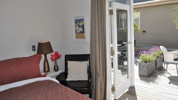 A hotel room with a bed, a chair, a table, and a view of the outdoor area with plants and a patio. - Queenstown House Boutique Bed and Breakfast and Apartments (Queenstown)