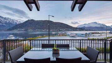 A balcony with a table and chairs, overlooking a body of water and mountains.