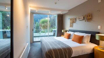 A modern hotel room with a large bed, two bedside tables, a view of the outdoors, and a balcony with a sliding door.