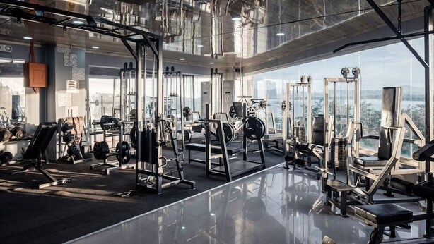Een moderne sportschool met diverse gewichthefapparaten, grote ramen en een hoge plafond.