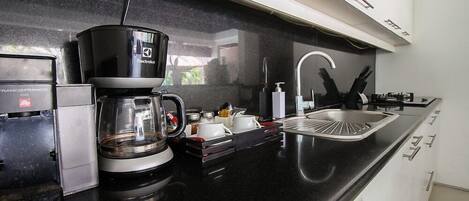 A modern kitchen with a black countertop, a coffee maker, a sink, and a dishwasher.