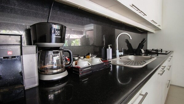A modern kitchen with a black countertop, a coffee maker, a sink, and a dishwasher. - Chandra Bali Villas (Seminyak)