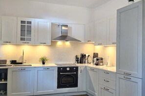 A modern kitchen with white cabinetry, a stainless steel range hood, and a built-in oven. - Blue Nest apartment (Locarno)