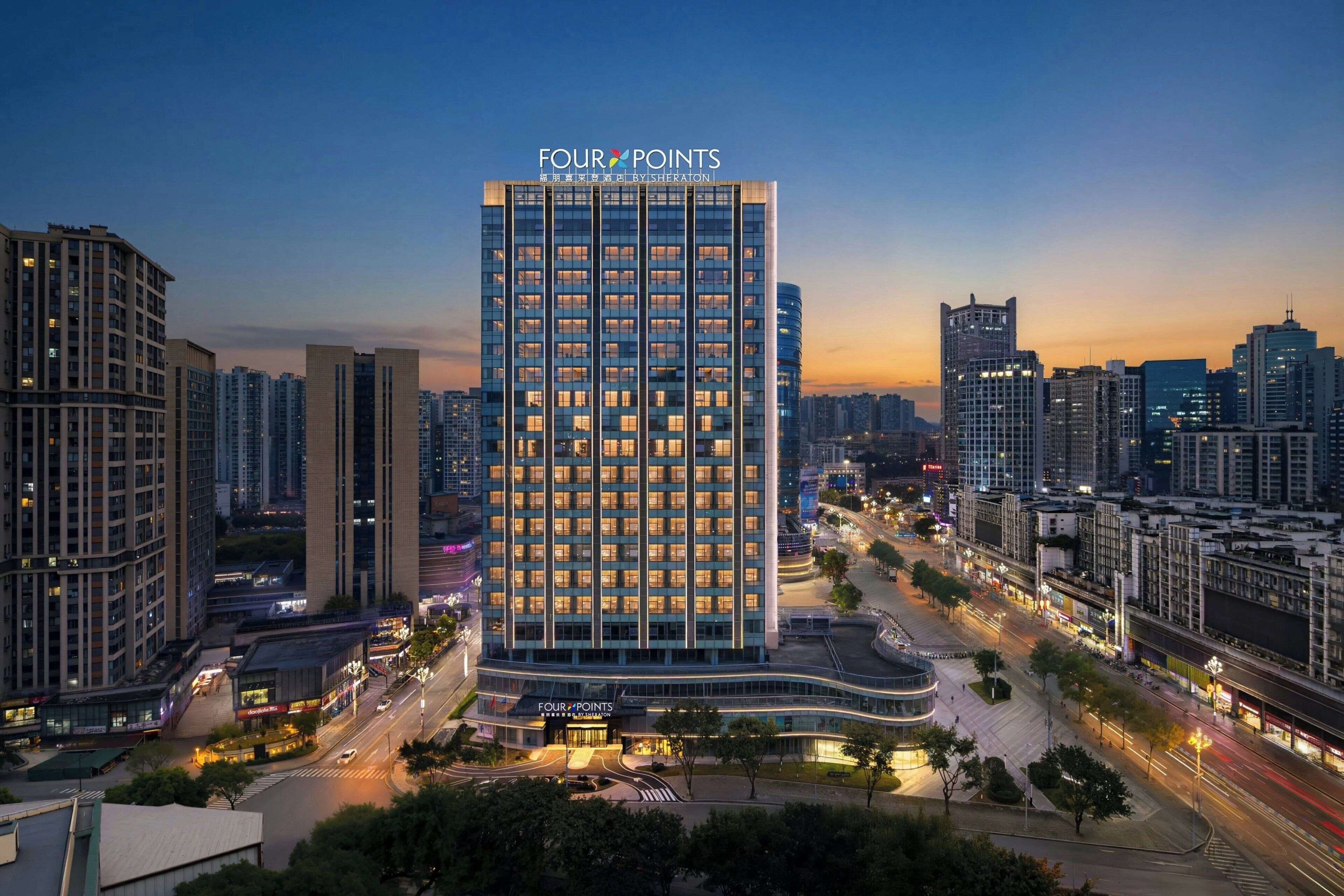 A high-rise hotel with a modern glass facade, surrounded by a cityscape at dusk.
