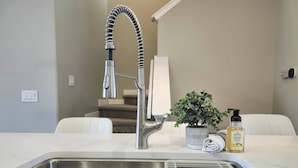 A modern kitchen with a stainless steel sink, a high-arc faucet, a potted plant, and a bottle of hand soap.