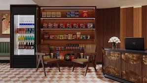 Un vestíbulo de hotel con suelo a cuadros, un refrigerador lleno de bebidas, una estantería con aperitivos y un ordenador portátil sobre un mueble de madera.