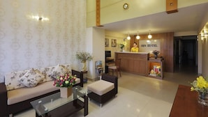 Un vestíbulo de hotel con un sofá, una mesa de centro de vidrio, un mostrador de recepción y un cartel que dice "SEN HOTEL".