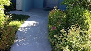 A pathway leading to a door, flanked by greenery and a building with a blue exterior. - Joia Luxury Hotel Luxury Apartments (Brusaporto)