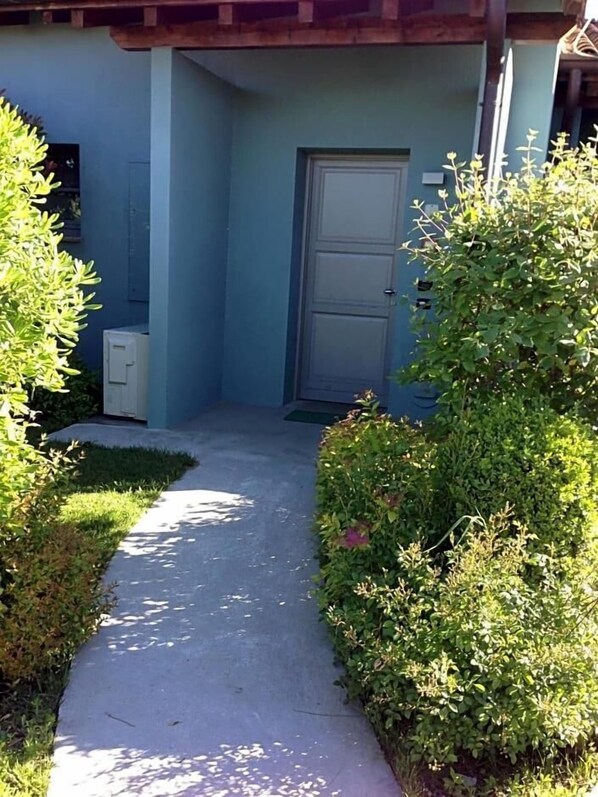 A pathway leading to a door, flanked by greenery and a building with a blue exterior. - Joia Luxury Hotel Luxury Apartments (Brusaporto)