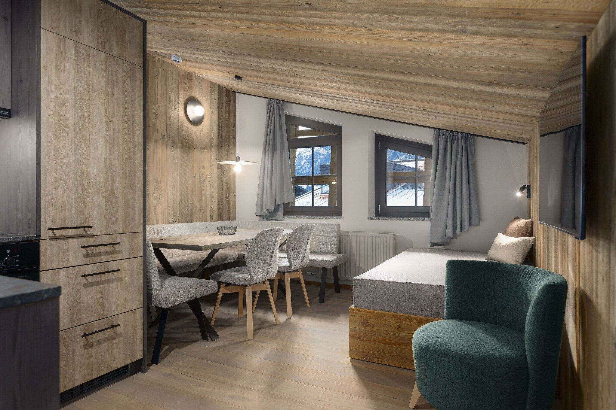 Une chambre moderne et compacte, dotée d’un plafond en bois, d’un lit, d’un bureau avec des chaises et d’une télévision.