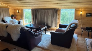 Een gezellig cabin interieur met een houten plafond, een zithoek, een eettafel en uitzicht op groen.