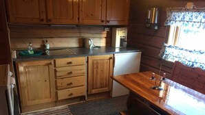 Een kleine keuken met houten kastjes, een koelkast en een eettafel met stoelen.