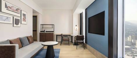 Una sala moderna con un sofá, una mesa de comedor y sillas, un televisor montado en la pared y un ventanal con vistas a la ciudad.