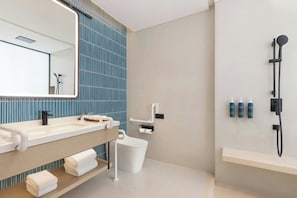 A modern bathroom with a large mirror, dual sinks, a toilet, a shower, and a towel rack.
