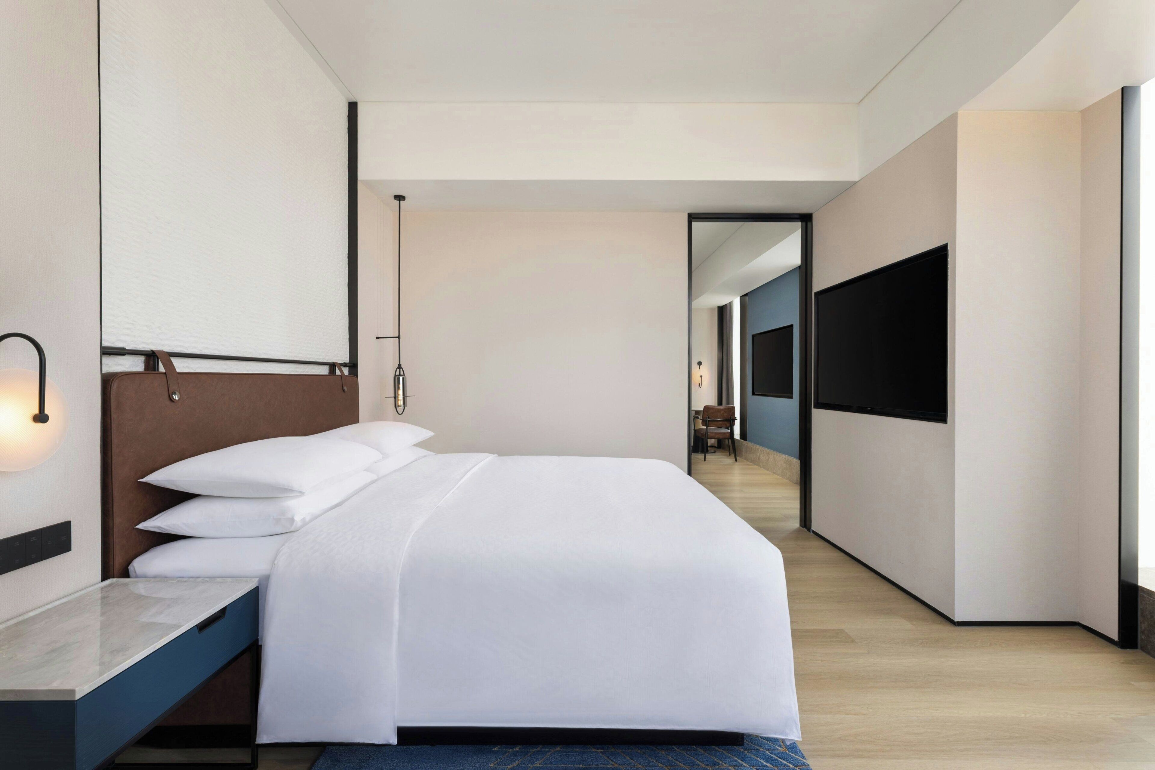A modern hotel room with a large bed, a desk, and a TV.