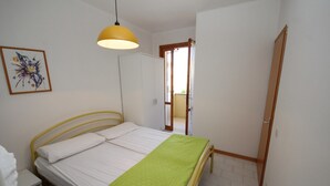 Een slaapkamer met een bed, nachtkastje, hanglamp, kledingkast en een deur die naar een andere kamer leidt.