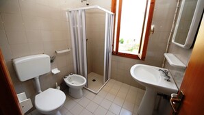 Een badkamer met toilet, bidet, douchecabine, wastafel en een raam.