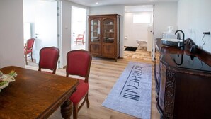 Een eetgedeelte met een houten tafel en rode stoelen, een kast met glazen deuren, en een keuken met een spoelbak en aanrecht.