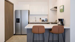 Une cuisine moderne équipée d’un réfrigérateur en acier inoxydable, d’un plan de travail blanc, de deux tabourets de bar et d’une machine à café.