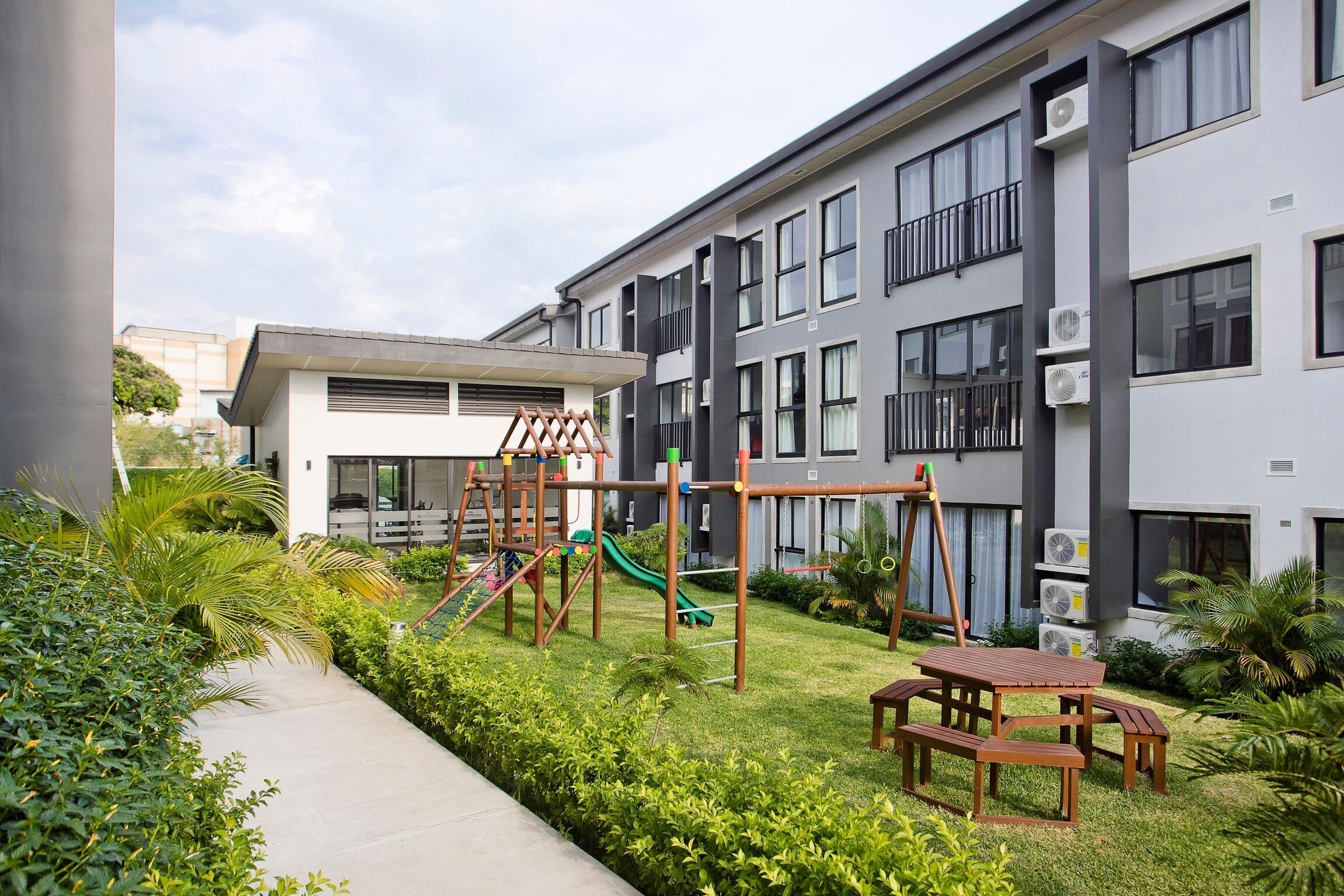 Un immeuble d’appartements moderne doté d’un espace de jeux pour enfants, comprenant un toboggan et des structures d’escalade.