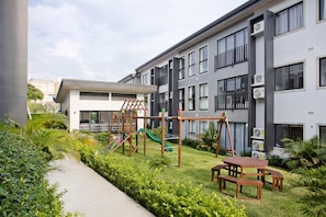Un immeuble d’appartements moderne doté d’un espace de jeux pour enfants, comprenant un toboggan et des structures d’escalade.