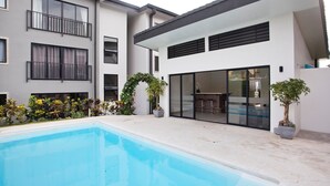 A modern residential building with a swimming pool, outdoor seating, and a variety of plants.