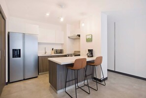 Una cocina moderna con un refrigerador de acero inoxidable, un microondas, una estufa y una cafetera. Hay dos taburetes de bar en la isla.