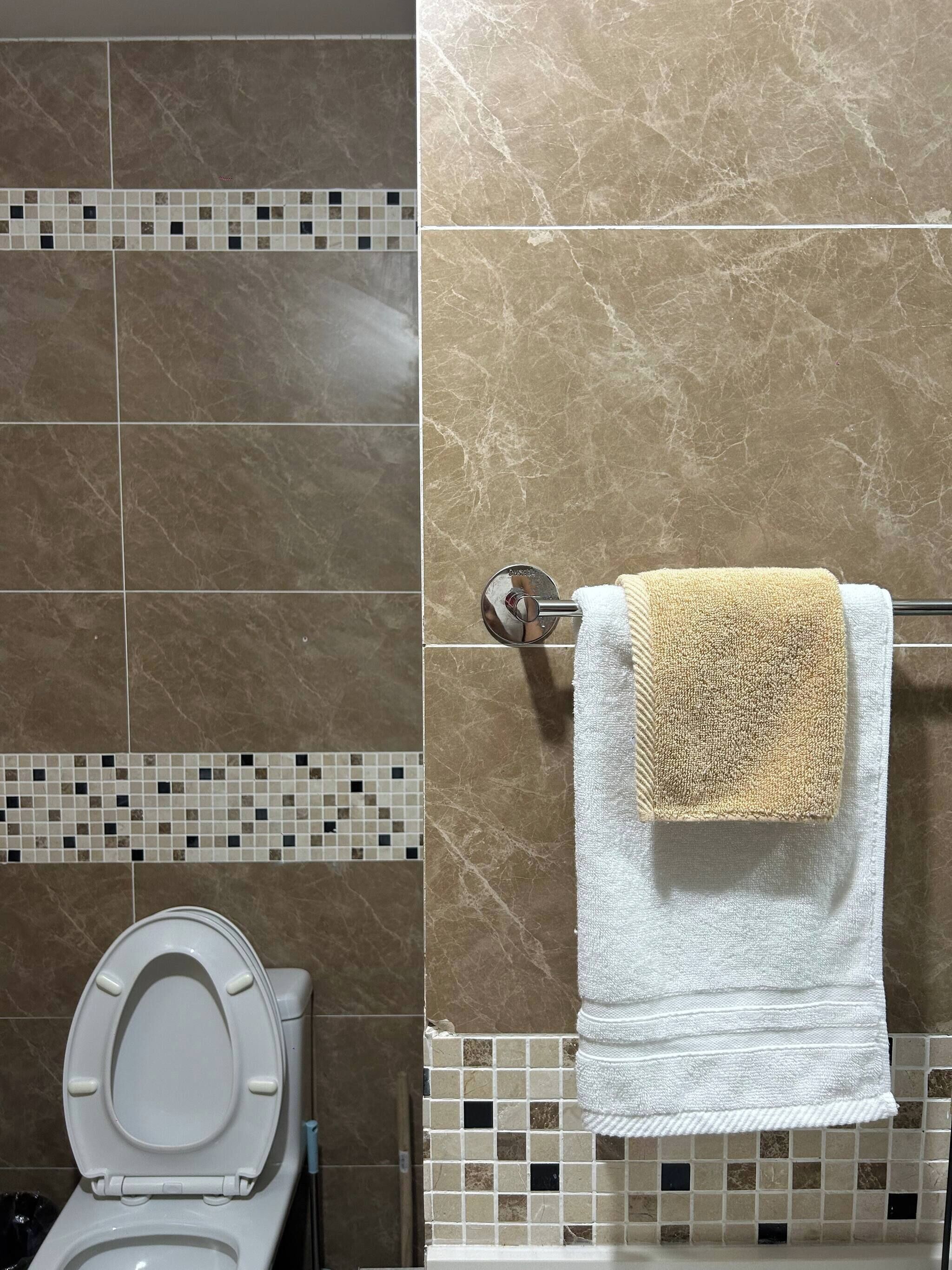 Un baño con inodoro, un perchero con una toalla blanca y beige, y paredes con diseño que imita el mármol.