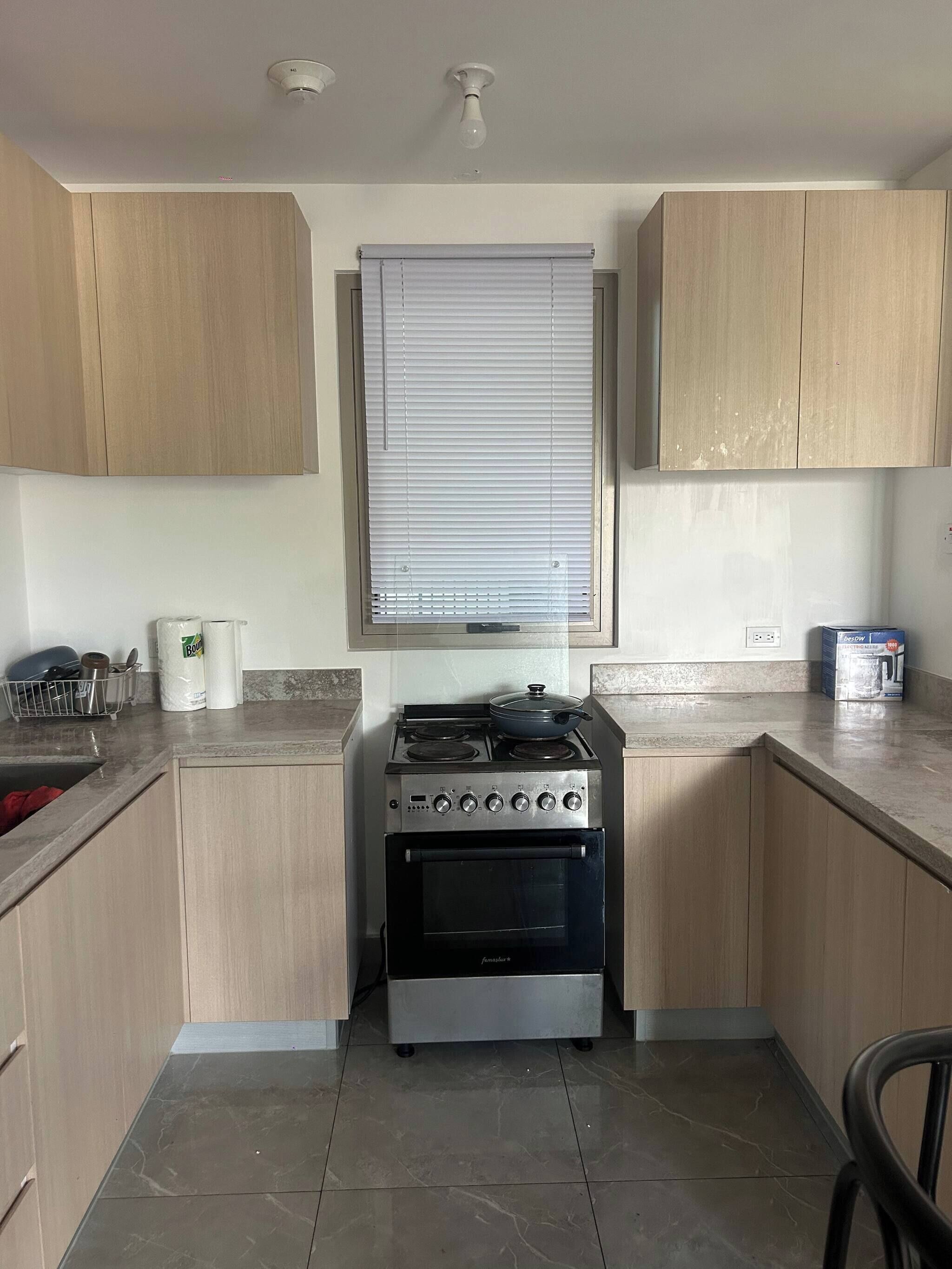 A compact kitchen with wooden cabinets, a gas stove, an oven, and a window with blinds.