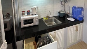 A kitchen with white cabinets, a black countertop, a microwave, a sink, and a dish rack. - Cozy 1-Bedroom House Rental in Hermosa, Philippines (Hermosa)