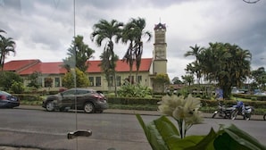 A street view with parked cars, a building with a red roof, and a tower structure. - La Fortuna Downtown Boutique Hotel (La Fortuna)