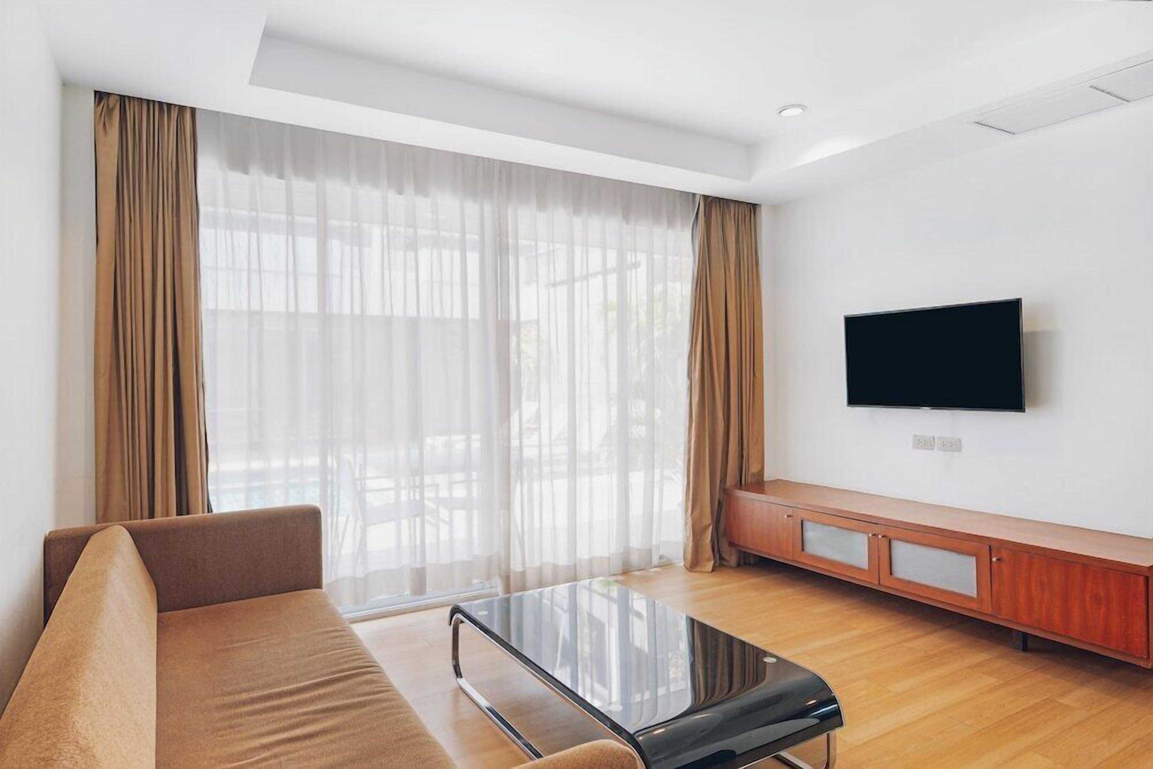 A modern living room with a sofa, a glass coffee table, a TV mounted on the wall, and a wooden cabinet.