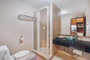 Een moderne badkamer met een douchecabine van glas, een toilet, een wastafel met een glazen kom en een spiegel boven de wastafel.
