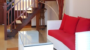A living room with a wooden staircase, a white sofa with red cushions, and a glass coffee table. - Chateau Dale Boutique Residence (Pattaya)