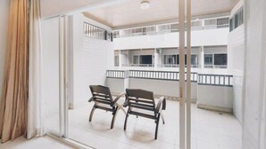 A balcony with two wooden chairs, white walls, and a view of the building's interior. - Chateau Dale Boutique Residence (Pattaya)