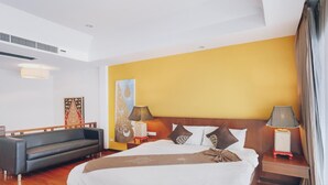 A hotel room with a large bed, two bedside tables with lamps, a sofa, and a wooden headboard. - Chateau Dale Boutique Residence (Pattaya)