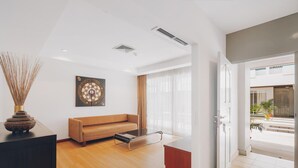 A modern living room with a sofa, a coffee table, and a decorative vase. There is a door leading to an outdoor area with plants. - Chateau Dale Boutique Residence (Pattaya)
