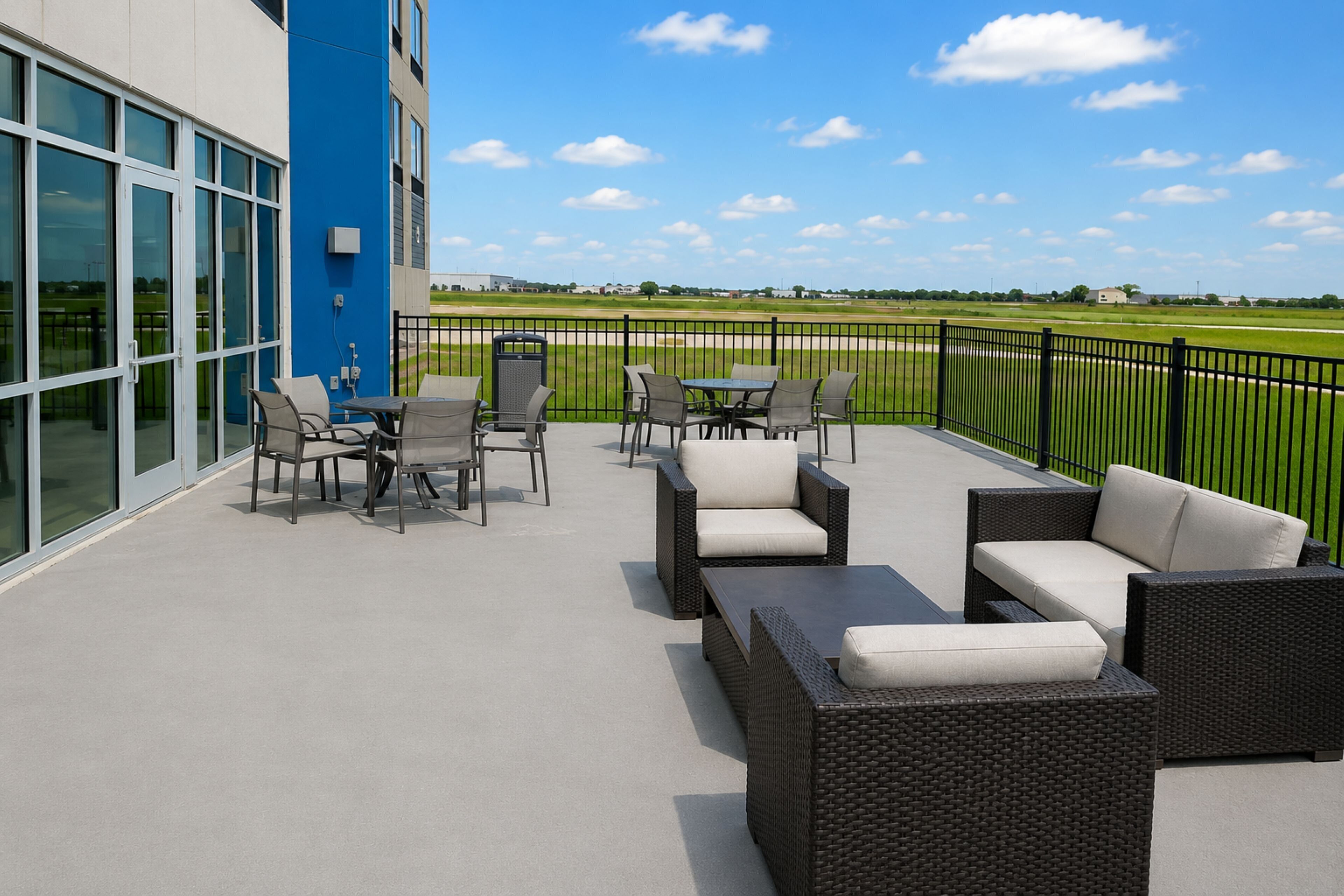 An outdoor patio with wicker furniture and a view of a green field.