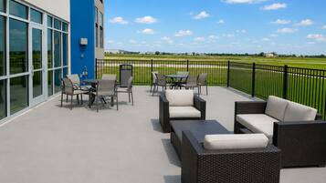 An outdoor patio with wicker furniture and a view of a green field.