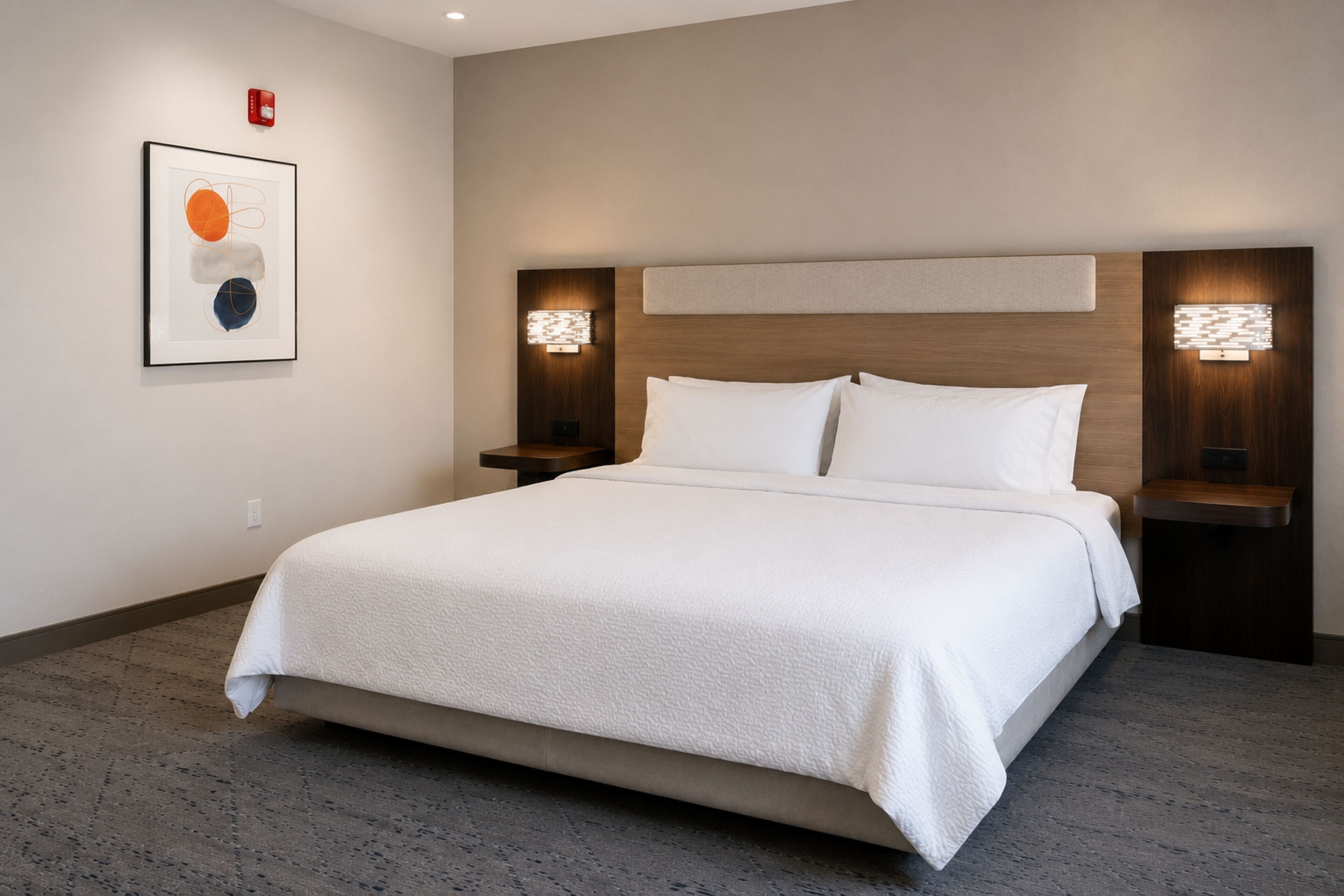 Habitación de hotel con una cama grande, dos mesitas de noche, un cabecero y una lámpara fijada a la pared.