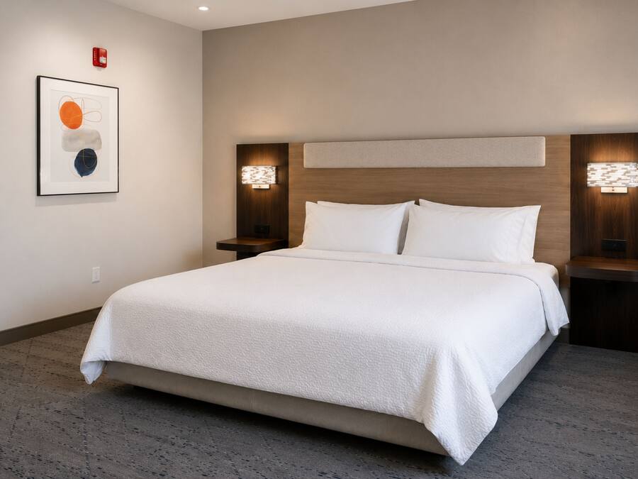 Habitación de hotel con una cama grande, dos mesitas de noche, un cabecero y una lámpara fijada a la pared.