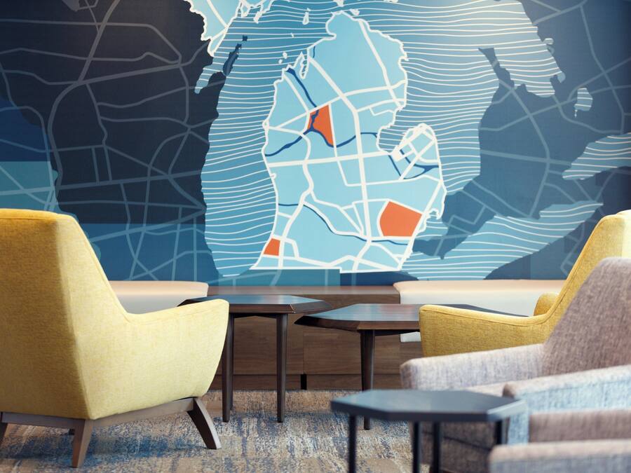 A modern lounge area with two yellow armchairs and a gray armchair, a wooden coffee table, and a large abstract wall art piece.