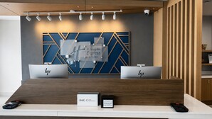 Un comptoir d’accueil d’hôtel au design moderne, comprenant une œuvre d’art murale aux motifs géométriques, deux guichets d’accueil et un panneau indiquant le programme de fidélité IHG Rewards.