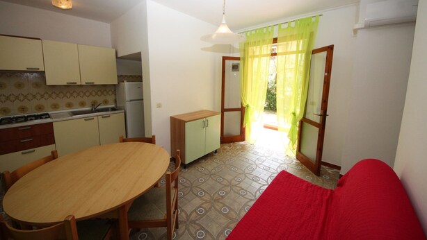 A compact kitchen with a dining area, a small cabinet, and a window with curtains. - Rosolina Mare Apartment Near Sea (Rosolina Mare RO)