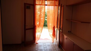 A hallway with a door leading to a garden, a tiled floor, and a wooden door frame. - Rosolina Mare Apartment Near Sea (Rosolina Mare RO)