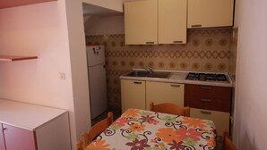 A small kitchen with a refrigerator, sink, and stove. There is a dining table with chairs and a floral tablecloth. - Rosolina Mare Apartment Near Sea (Rosolina Mare RO)