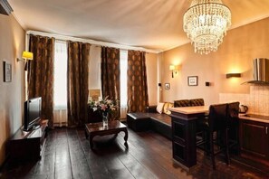 A room with a television, a sofa, a small table with flowers, a bar area, and a chandelier. - Apartamenty Torun Rynek Staromiejski (Torun)