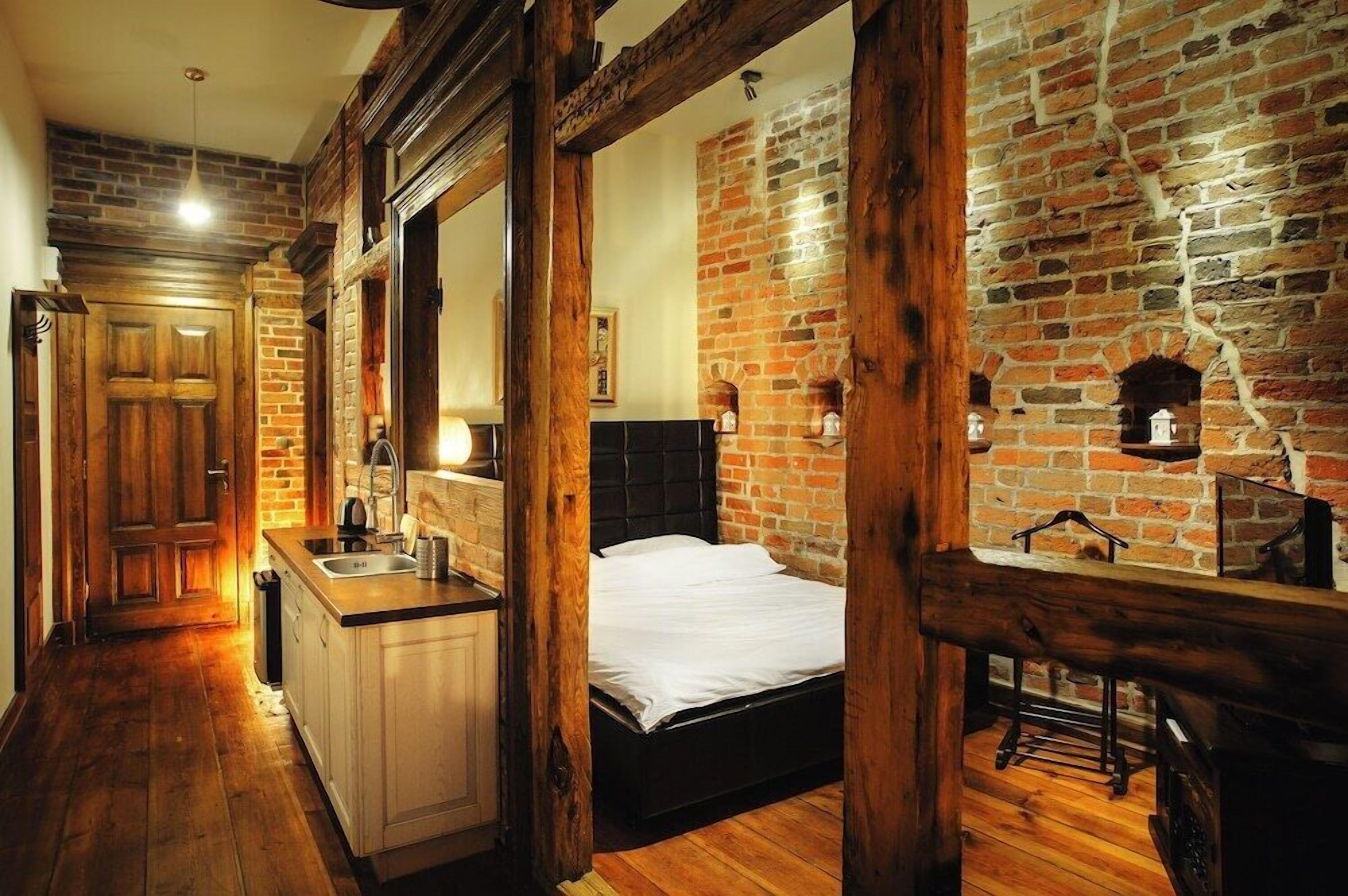 Un dormitorio con pared de ladrillo, vigas de madera, cama, mesita de noche y cómoda.