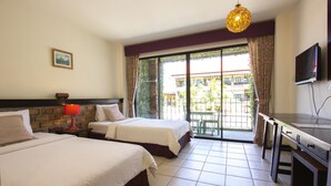 A hotel room with two beds, a TV, a desk, and a balcony with a view of buildings and greenery. - Tony Lodge (Takua Pa)