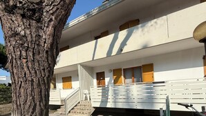 Ein zweistöckiges Gebäude mit weißer Fassade, Holztüren und einer Treppe, die zum Eingang führt.